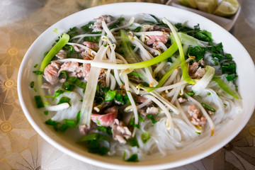 A traditional Vietnamese soup Pho Bo, with raw beef, green onions, soy sprouts