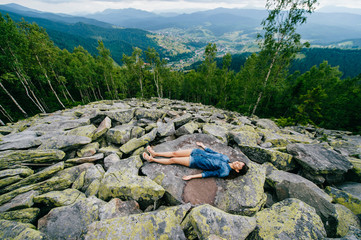 Young, lonely traveler girl lying at rocky stones high at mountains and meditating.  Unity of human...