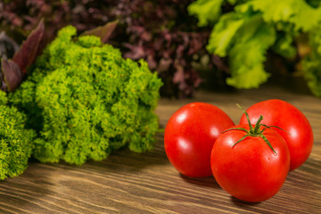 Fresh ripe tomatoes on a wooden table with a green salad on the background. Fresh vegetables.