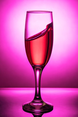 Splash of pink wine to the edge in a glass goblet on a pink background with a gradient spot