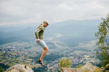 Traveler tourist sportsman in athletic footwear jumping from stone at top of mountain on high altitude outdoor. Greatness of nature landscape. Wellness, healthy lifestyle. Wild terrain in countryside.