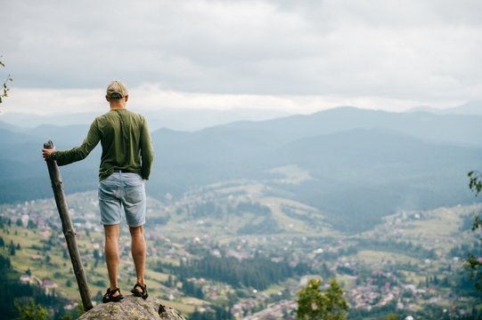 Strong man with wooden staff stick looking far at horizon. Primal leader. Masculine power. Discover, coquer. Kingdom lord. Edge of world. Nature spirit salutation. Rude strength. Reaching highest peak