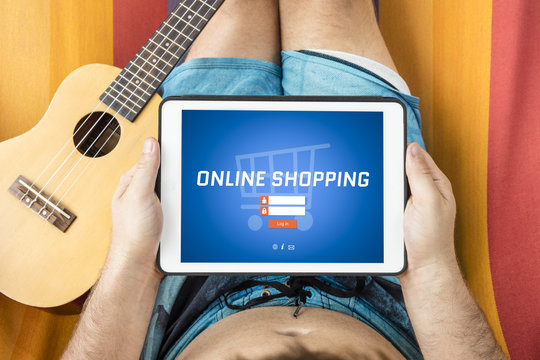 Young man visiting an online shopping website with tablet device, lying on a hammock