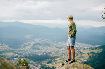 Fototapeta na wymiar Lonely traveler man in summer clothes standing on stone at top of carpathian mountain and looking far from high altitude. Nature landscape with far horizon. Tourist resting in wild terrain on vacation
