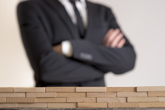 Businessman with folded arms with wall of wooden bricks infront of him