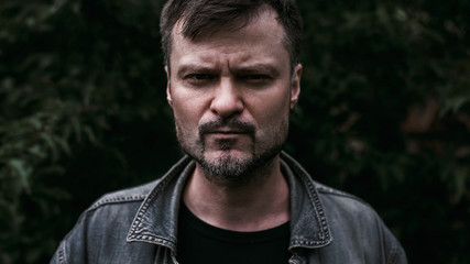 A strong man stands on a background of leaves and looking at the camera. Close-up portrait. Image film frame format 16:9.