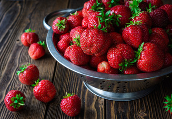 Colander with fresh strawberry and lying strawberry on wooden background