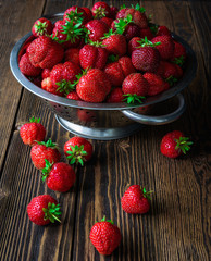 Colander with fresh strawberry and lying strawberry on wooden background