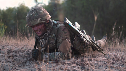 Man in military uniform with gun crawling alone on ground in field.