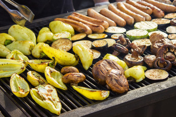 Assorted delicious grilled meats with vegetables over the barbecue on the charcoal. Sausages, steak, pepper, mushrooms, zucchini.