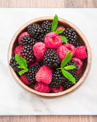 Wooden cup with fresh berries on white marble background