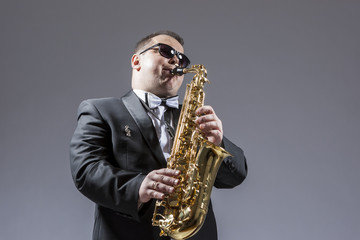 Fototapeta na wymiar Music Concepts. Portrait of Mature Expressive Caucasian Saxophone Player in Sunglasses Playing the Saxophone in Studio Environment.