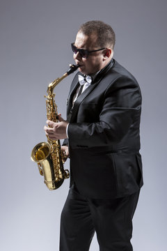 Music Ideas and Concepts. Portrait of Caucasian  Saxophone Player in Sunglasses Playing the Instrument in Studio Environment.