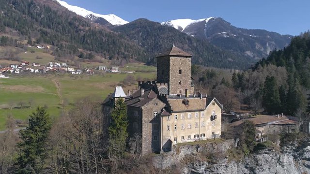 Aerial footage of a castle on the cliff in a valley with mountains in the background. Shot in Switzerland in 4k quality.