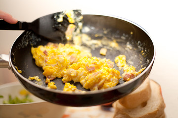 Scrambled eggs and bacon in metal black cooking pan Italian Food Made in Italy with bread and salad on table