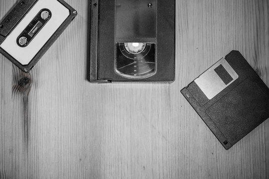retro vintage storage media from 90's : audio tape, video cassette vhs, floppy disk on wooden background in black and white