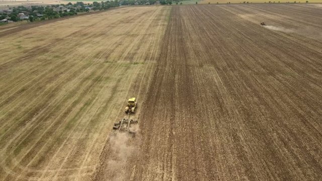 Impressive aerial shot of a farm tractor drawing a spike and a disc harrows to remove wheat straw and to do a  tillage in Eastern Europe in a sunny day in summer. The drone is flying after the tractor