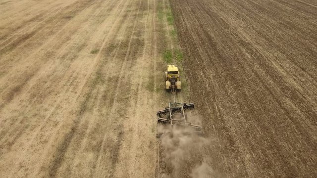 Amazing aerial shot of a big tractor drawing a spike and a disc harrows to remove wheat straw and to do a  tillage in Eastern Europe in a sunny day in summer. The drone is flying after the tractor