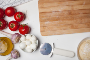 Wooden cutting Board with ingredients for homemade pizza on a white table