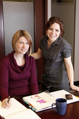 Two attractive businesswomen smile while working on project