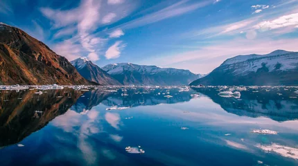 Fotobehang Wolken weerspiegeld in het blauwe water van de Groenlandse fjord, omringd door besneeuwde toppen. © Di