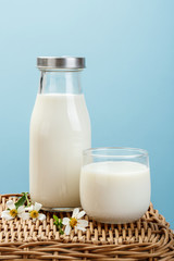 A bottle of milk and glass of milk on a wicker table on a blue background