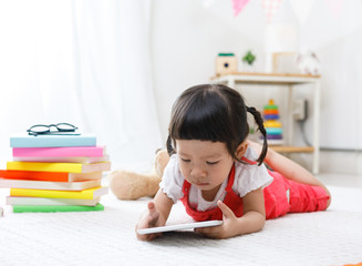 Naklejka premium Preschooler girl plaing tablet. Cute child reading with teddy bear. Little girl having fun indoors at home, kindergarten or