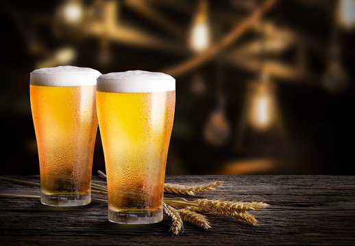 Glasses of light beer with barley at bar. Two glass of beer with wheat on wooden table