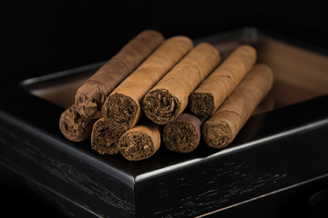 RIch smelling cigars invite a late evening smoke with friends. Multiple cigars above a black humidor and a black background