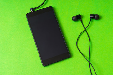 Obraz premium Mobile phone with headphones on green background