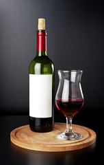 Red wine bottle with wine glass on wooden cutting board isolated on black background. Front view.