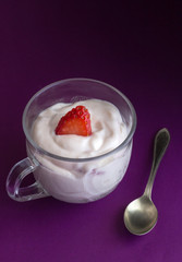 Natural strawberry yoghurt in small glass cup and little spoon on purple background close up