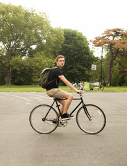 Naklejka premium Full figure shot of modern Caucasian college student riding bike in the park