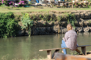 Fototapeta premium Lonely woman sitting on wooden bench at the riverside.
