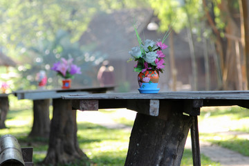 Rose artificial flower in the pot on wooden table in front of cottage resort.