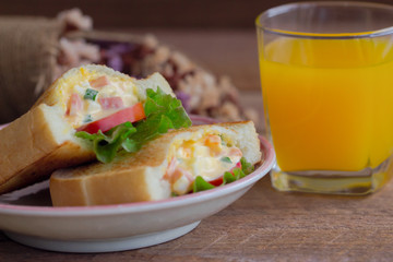 Pocket sandwich for breakfast or lunch. Homemade sandwich with hard boiled eggs and mayonnaise decorated by lettuce and tomato. Baked sandwich on lovely plate serve with orange juice on wood table.