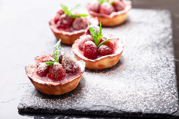 Homemade strawberries tarts with powdered sugar on slate plate, black background. Close up.