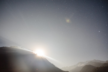 Moon rising with ray light behide the mountain with little snow on the top and moving cloud in the blue color night with stars in winter at Lachung in North Sikkim, India.