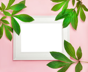 Fototapeta premium white wooden frame on pink background decorated with green leaves, blank space for a text. Top view, flat lay