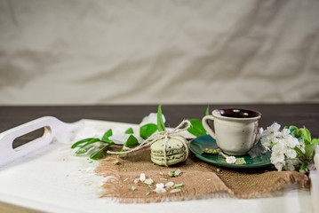 Obraz na płótnie Canvas A cup of coffee on a white tray with branch of blossomed cherry and monstera leaf