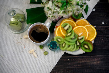Morning tea or coffee with orange and kiwies slices and green macaroons on a white blanket with cherry blossom
