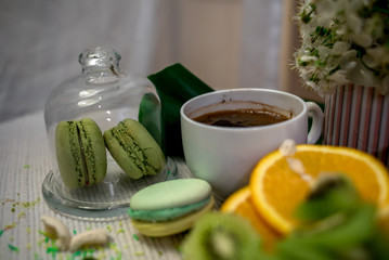 Morning tea or coffee with orange and kiwies slices and green macaroons on a white blanket with cherry blossom