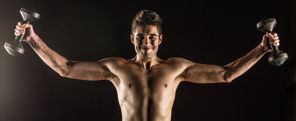 Man stretching arms outward doing a Standing Dumbbell Chest Fly. Studio composite over black.