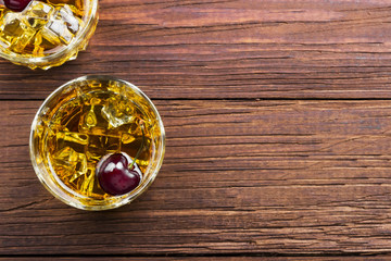 Cocktail from whisky with cherry in two glasses on a wooden background. Top view, copy space. Food background
