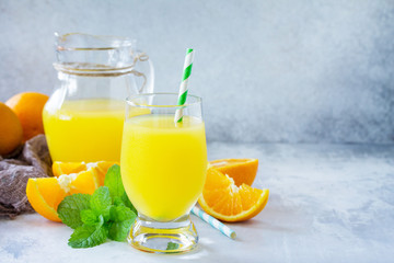 Obraz na płótnie Canvas A refreshing summer drink with orange juice, fresh oranges and mint on a gray stone or slate background. The concept of healthy and dietary nutrition. Copy space.