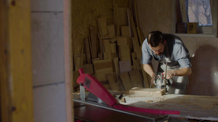 20s bearded woodworker works with brashing machine at sunny day in workshop