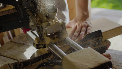 Close up hands of carpenter neg wooden plank using circular saw. flying sawdust