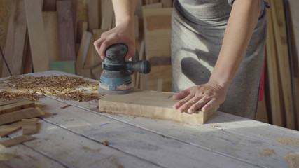 Hands of woodworker carpenter grinding wooden plank in backlight using machine