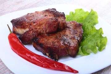 Steak of grilled meat and chili pepper with tomato, lettuce leaves on white plate.