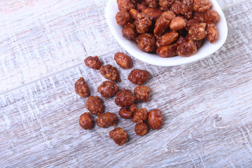 Sugared Hazelnuts in a white bowl on a wooden background. Hazelnuts in sugar glaze. Selective focus.